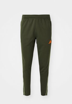 Olivengrønne træningsbukser med elastisk talje, der har et orange Adidas-logo og sidelommer. Fremstillet af glat, let materiale.