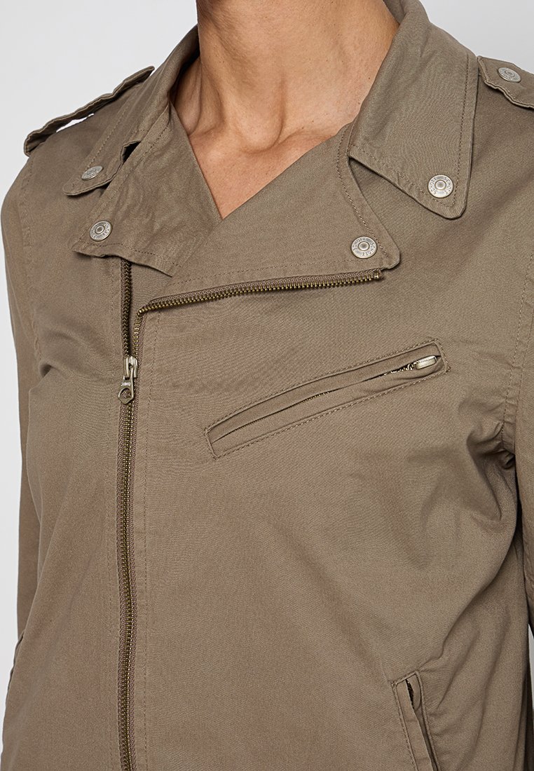 Veste kaki au design ajusté, avec une fermeture à glissière diagonale, une poche poitrine zippée et des épaulettes à boutons.