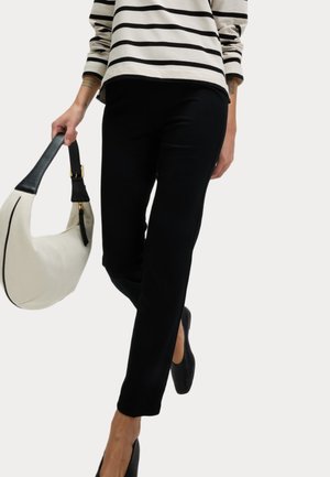 Pantaloni neri slim-fit con una texture liscia, abbinati a una maglietta a righe e a una borsa a mezzaluna beige, con manico nero.