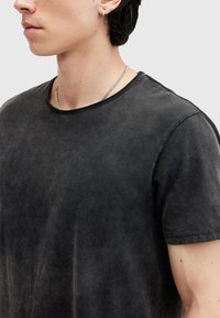Schwarzes T-Shirt mit kurzen Ärmeln aus einem verblassten, strukturierten Stoff; hat einen runden Ausschnitt und einen leicht übergroßen Schnitt, mit einer glatten Oberfläche.