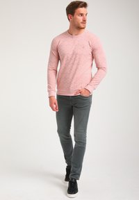 Sweatshirt rose clair avec un motif texturé, manches longues, poignets côtelés et un design bleu marine. Associé à un jean gris ajusté et des baskets noires.