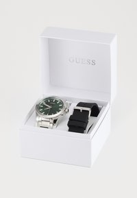 Orologio argento con quadrante verde e bracciale in acciaio inox, abbinato a un cinturino in silicone nero, presentato in una scatola bianca.