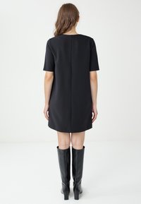 Abito dritto nero con maniche corte e cucitura posteriore, abbinato a stivali neri al ginocchio. Tessuto liscio con una silhouette semplice e classica.