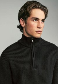 Schwarzer Rippstrickpullover mit hohem Kragen und halbem Reißverschluss. Das strukturierte Material und die taillierte Passform sorgen für eine moderne Silhouette.