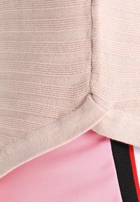 Baumwollmischung Oberteil in hellem Beige mit horizontaler Ripptextur, das einen leicht abgerundeten Saum aufweist, der pinkfarbenen Stoff darunter überlappt.