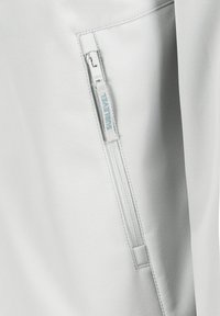 Hellegrau weiche Shell-Bekleidung mit einer Reißverschlusstasche und einem dezenten blauen Reißverschlusszug, glatter Textur und klaren Designlinien.