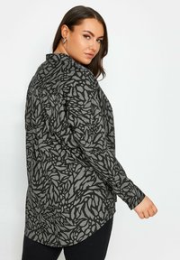 Long-sleeve shirt in black with a textured gray organic leaf pattern, featuring a button-up collar and a curved hemline.