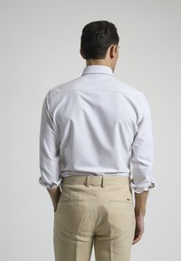 Camisa blanca a rayas con botones y mangas enrolladas, combinada con pantalones beige con bolsillos traseros. Diseño minimalista, tejido suave.