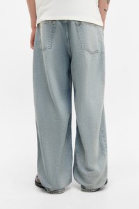 Lyseblå, vide jeans med falmet struktur, der har to baglommer og en lige kant. Båret med mørke sko.