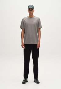 Sivá bavlnená tričko s voľným strihom, skombinované s čiernymi nohavicami. Tmavozelená čiapka s bielym textom. Čierne tenisky dotvárajú outfit.