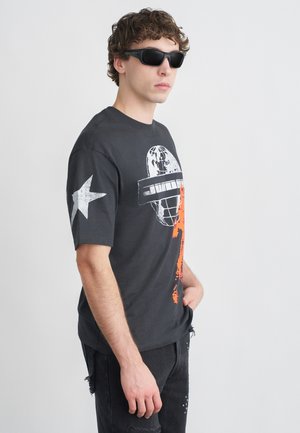 Musta puuvillainen lyhythihainen t-paita, jossa valko-oranssi graafinen kuvio ja valkoinen tähti vasemmassa hihassa. Yhdistetty mustiin farkkuihin.