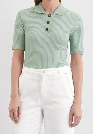 Myntegrøn ribbet poloshirt med korte ærmer, tre mørke knapper og krave, kombineret med hvide bukser med høj talje.