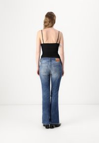 Jeans svasati blu scuro in denim, con un classico design a cinque tasche e una toppa in pelle marrone sul retro. La vista posteriore mostra una vita aderente.