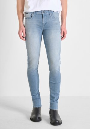Svijetloplave slim-fit traperice od denima, s izblijedjelim mrljama, pet džepova i kopčanjem na gumbe, uparen s crnim gležnjačama.