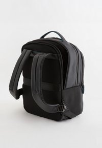 Mochila negra con respaldo de malla acolchada, correas ajustables duales y bolsillo lateral. Presenta un diseño elegante, con una textura suave y cierre de cremallera.