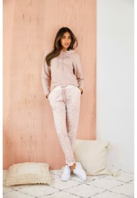 Sudadera rosa clara con bolsillo frontal y cordones, combinada con pantalones crema de patrón de cebra y zapatillas blancas. Tela suave y corte casual.