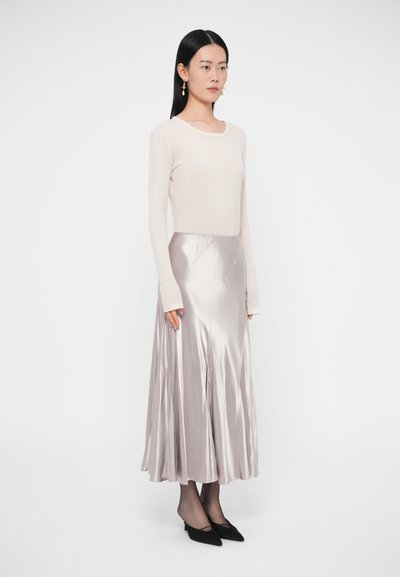 Testhez simuló, világos bézs színű hosszú ujjú felső, amelyet egy légies, fémes ezüst szatén midi szoknyával és fekete hegyes orrú magassarkúval párosítottak.