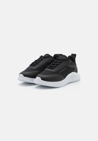 Scarpe da ginnastica nere con tomaia texture e suola in gomma liscia. Le caratteristiche includono lacci, suola bianca a contrasto e marchio sul lato.