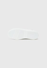 Semelle de sneakers en caoutchouc blanc avec une surface texturée, présentant des rainures horizontales, des bords arrondis et un logo embossé près du talon.