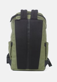 Olivgrüner Rucksack mit einem schwarzen Mesh-Rückenteil, gepolsterten Schultergurten und einem Reißverschluss oben. Verfügt über Seitentaschen und eine schlanke rechteckige Form.