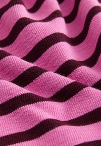 Gros plan sur un tissu tricoté rose avec des rayures horizontales sombres en relief, créant un motif ondulé et une surface texturée.