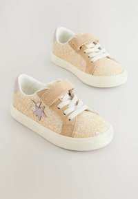Baskets beige scintillantes avec une texture douce, lacets blancs, une sangle Velcro et un accent étoile lavande sur le côté. Semelle en caoutchouc.