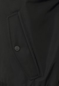 Giacca nera dal design elegante presenta un bottone con "HUGO", una tasca frontale e un tessuto liscio e strutturato.