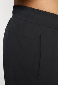 Calções atléticos pretos com uma cintura elástica, featuring um bolso lateral e textura suave, projetados para conforto e flexibilidade.