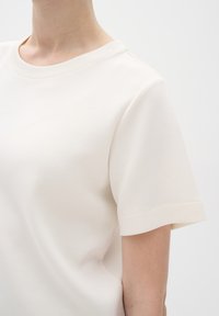 Cream cotton t-shirt featuring a round neckline and short sleeves with folded cuffs. The fabric has a smooth, soft texture.