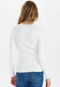 Weißes, geripptes Langarmoberteil mit einer enganliegenden Passform, strukturierter Stoff und Rundhalsausschnitt, kombiniert mit blauen Jeans.