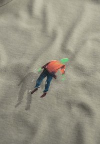 Grijze stof heeft een kleurrijke illustratie van een persoon in een rode shirt en blauwe broek, met groene accenten en een schaduweffect.