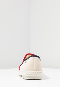 Canvas instapschoen in beige, met een rood en marineblauwe rand, een textuur oppervlak, geweven zool en een klein logodetail aan de zijkant.