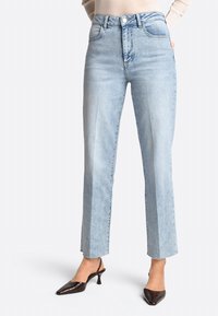 Jeans de tiro alto color azul claro con un diseño de pierna recta, que cuentan con bolsillos laterales y un dobladillo sin rematar. Combinados con zapatos de tacón marrón oscuro.