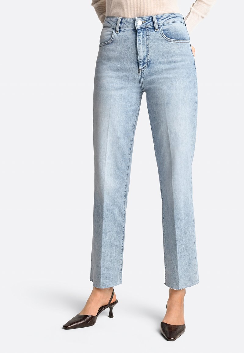 Jeans de tiro alto color azul claro con un diseño de pierna recta, que cuentan con bolsillos laterales y un dobladillo sin rematar. Combinados con zapatos de tacón marrón oscuro.