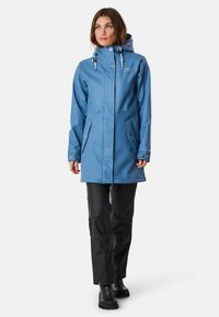 Niebieska wodoodporna parka z kapturem, z przednimi kieszeniami, regulowanymi mankietami i gładkim wykończeniem. W połączeniu z czarnymi wodoodpornymi spodniami.