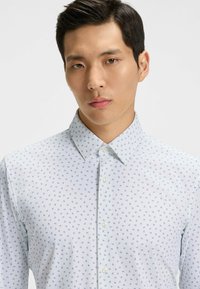 Vit skjorta med knappar och ett subtilt blått mönster. Lätt, mjukt tyg med klassisk krage och pärlknappar.