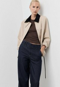 Beige bomberjack met een zwart corduroy kraag, gecombineerd met donkerblauwe hoge taille denim broeken. Soepele texturen en een ontspannen pasvorm.