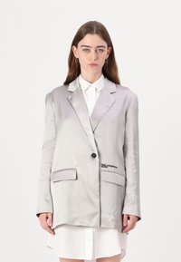 Sateng lys grå blazer med notched lapels, enkelt svart knapp, to front lommer, og brodert "Karl Lagerfeld Jeans" detalj.