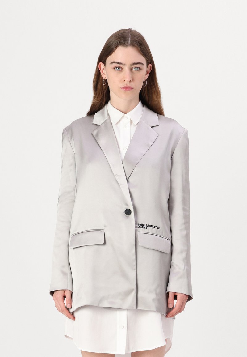 Sateng lys grå blazer med notched lapels, enkelt svart knapp, to front lommer, og brodert "Karl Lagerfeld Jeans" detalj.