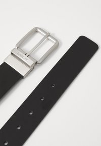 Zwarte leren riem met een geborsteld zilveren metalen gesp met "HUGO" gravure. De band heeft meerdere gaatjes voor aanpassing.