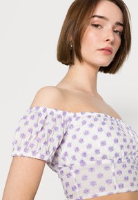 Top cropped branco com ombros à mostra, bordado floral púrpura, mangas bufantes elásticas e um design ajustado no corpete.