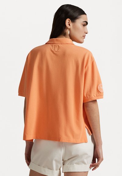 Polo tričko s krátkym rukávom a voľným strihom v jasne oranžovej bavne. Obsahuje golier, postranné rozparky a nášivku s logom na ľavom rukáve.