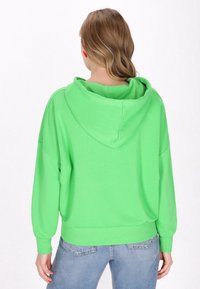 Felpa con cappuccio di un vivace verde, dal fit rilassato, con polsini e orlo a coste. Texture liscia, design informale e silhouette oversize.