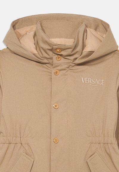 Beige huva jacka med guldfärgade knappar, broderad logotyp och elastisk midja. Slät, strukturerad tyg med sidofickor.