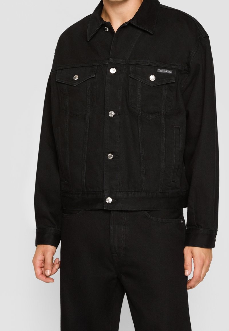 Svart denimjacka med knäppt framsida, två bröstfickor och klassisk krage. Har metallfästen och en kortad design.