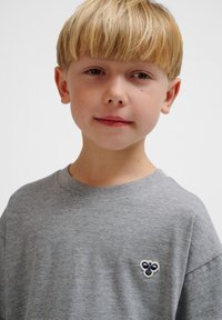 Graues Baumwoll-T-Shirt mit klassischem Rundhalsausschnitt und kleinem besticktem Bienenlogo in Blau und Weiß auf der linken Brustseite.