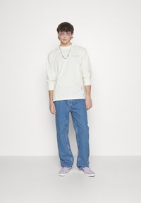 Cream long-sleeve shirt with "DICRIES" printed in light purple, paired with blue straight-leg jeans and purple checkerboard sneakers.