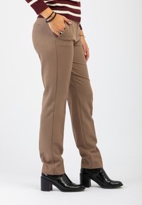 Pantaloni beige su misura con una texture liscia, dotati di tasche laterali e una vestibilità slim, abbinati a stivali alla caviglia neri con tacco.