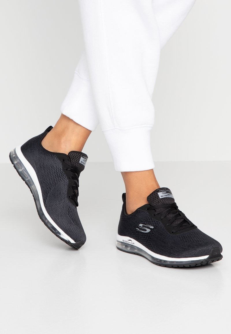 Svarta träningsskor med ett luftigt mesh-överkappa, snörningsdesign och en genomskinlig dämpad sula. Har vita accenter och logodetaljer.