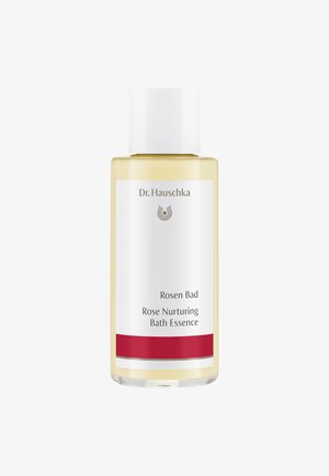 Bouteille en verre transparent contenant un liquide jaune, étiquetée "Rosen Bad Rose Nurturing Bath Essence", avec un bouchon blanc et un accent rouge à la base.